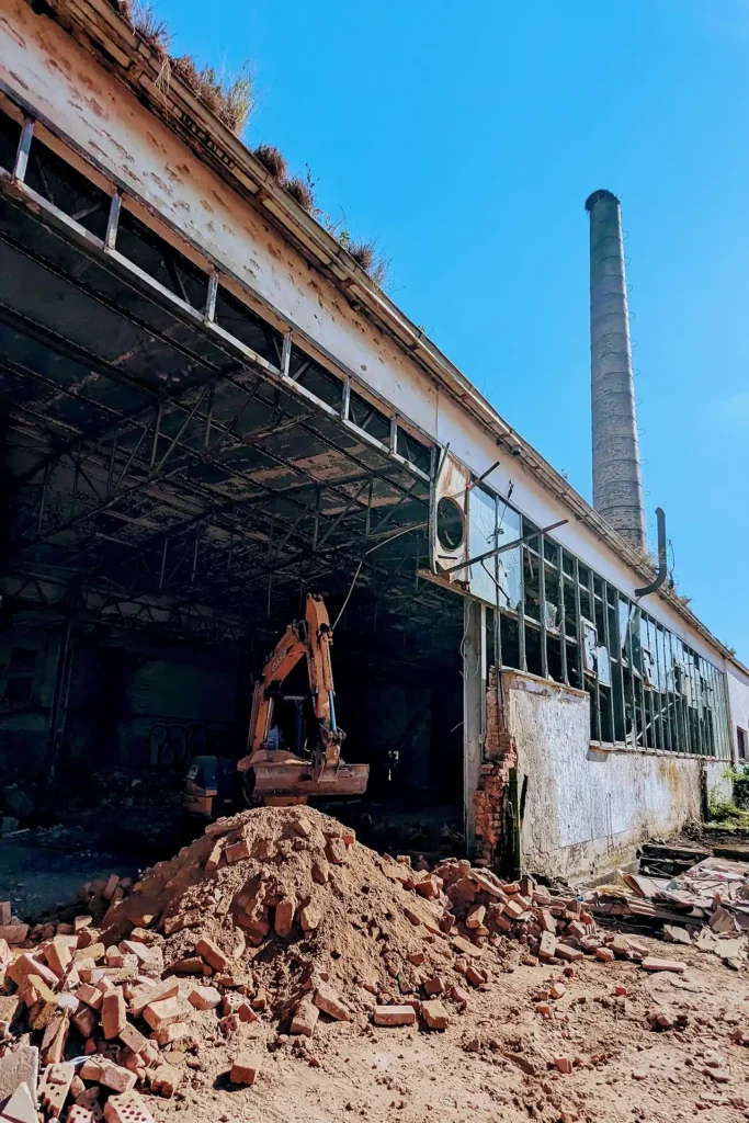 Blick in ein Gebäude des Molkereikomplexes Berka/Werra: Abbruch hat schon begonnen, im Vordergrund liegen Ziegel, man sieht einen kleinen Bagger und im Hintergrund den hohen Schornstein